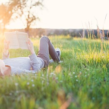 Frau liegt lesend mit einem Buch im Gras